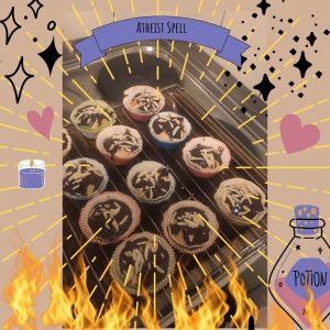12 Mandelcupcakes mit Schokoladenglasur, darum herum sind Comic Blitze, Sterne, Herzen, Kerzen, und einen Zaubertrank angeordnet. Unten hat es Flammen, die nach oben züngeln, oben einen Banner auf dem "Atheist Spell" steht.